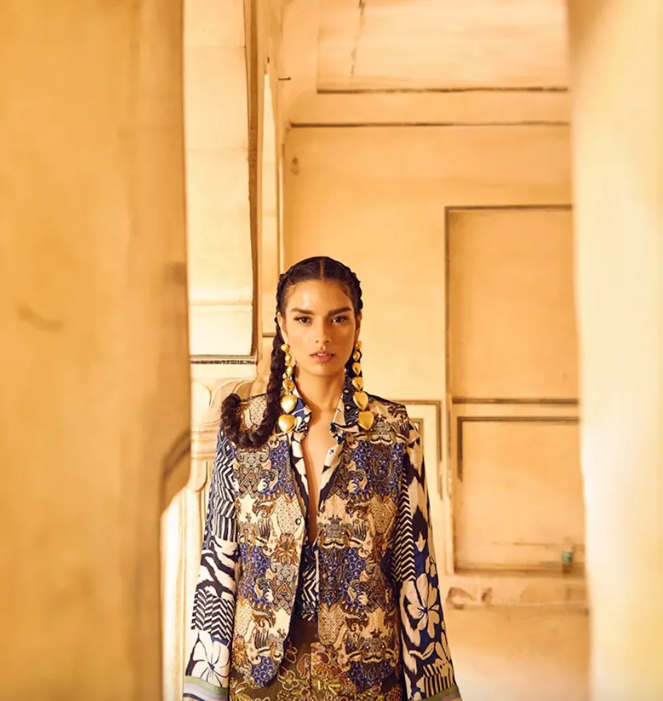 Model in braids wearing gold drop earrings, photographed against warm heritage architecture
